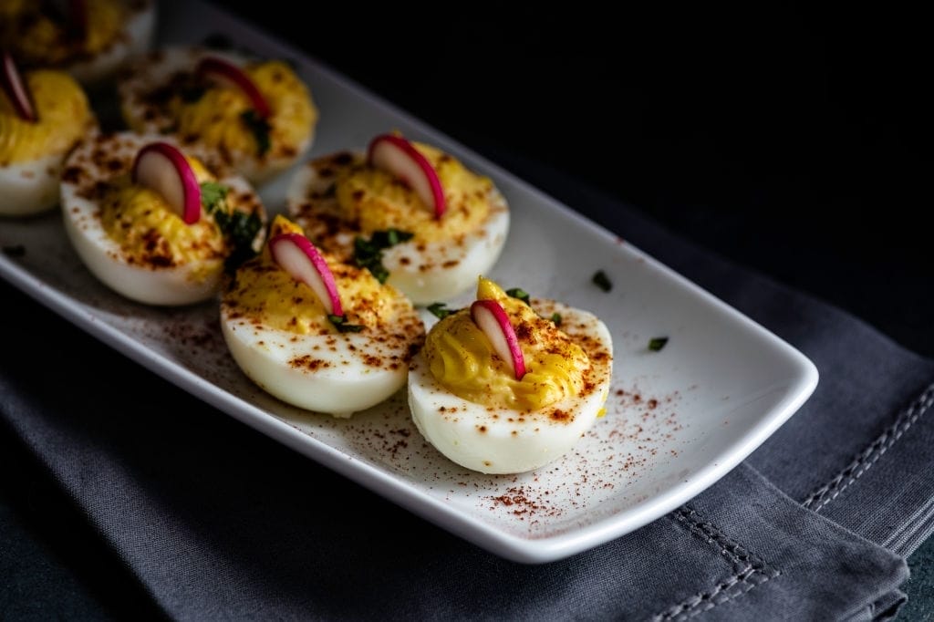 Keto deviled eggs on a white plate, garnished with paprika, radishes and chopped fresh basil