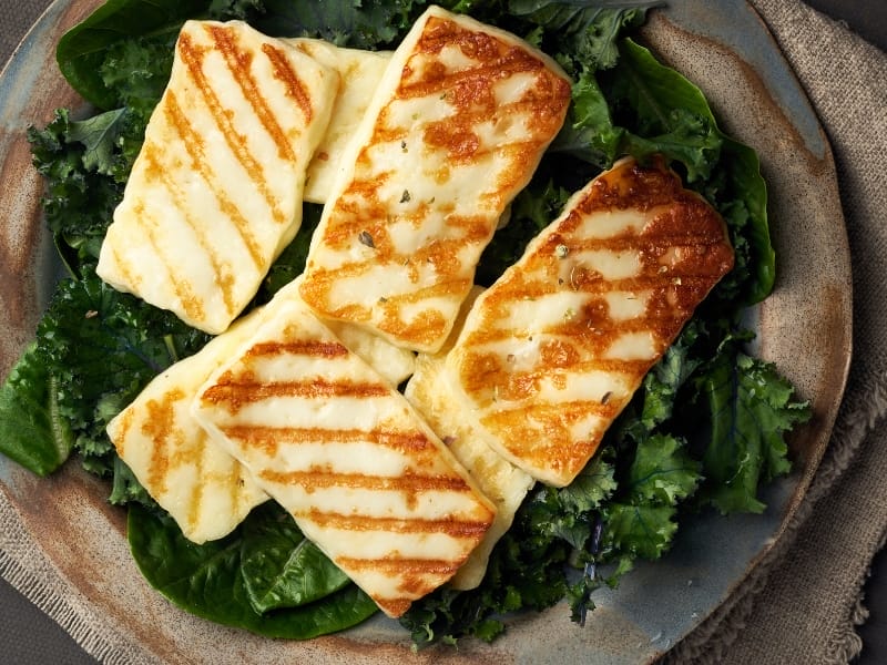 Melted halloumi cheese that has been grilled, on top of a serving of green leaf salad