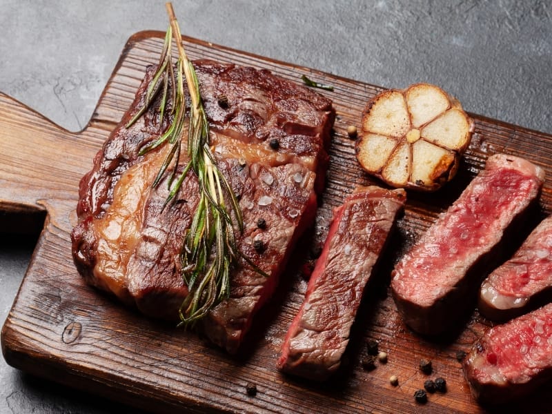 Grilled steak slices with rosemary and garlic on board.
