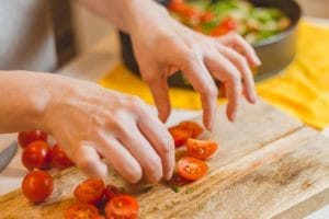 Slicing cherry tomatoes on wooden cutting board.